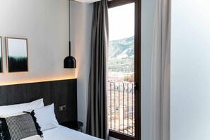 A hotel room with a bed, a bedside table, a hanging lamp, and a window with curtains.