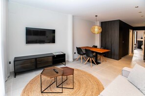 A modern living room with a flat-screen TV, a wooden dining table with chairs, a sofa, and a woven rug. - Mocho-rural-home Lonja B (Beceite)