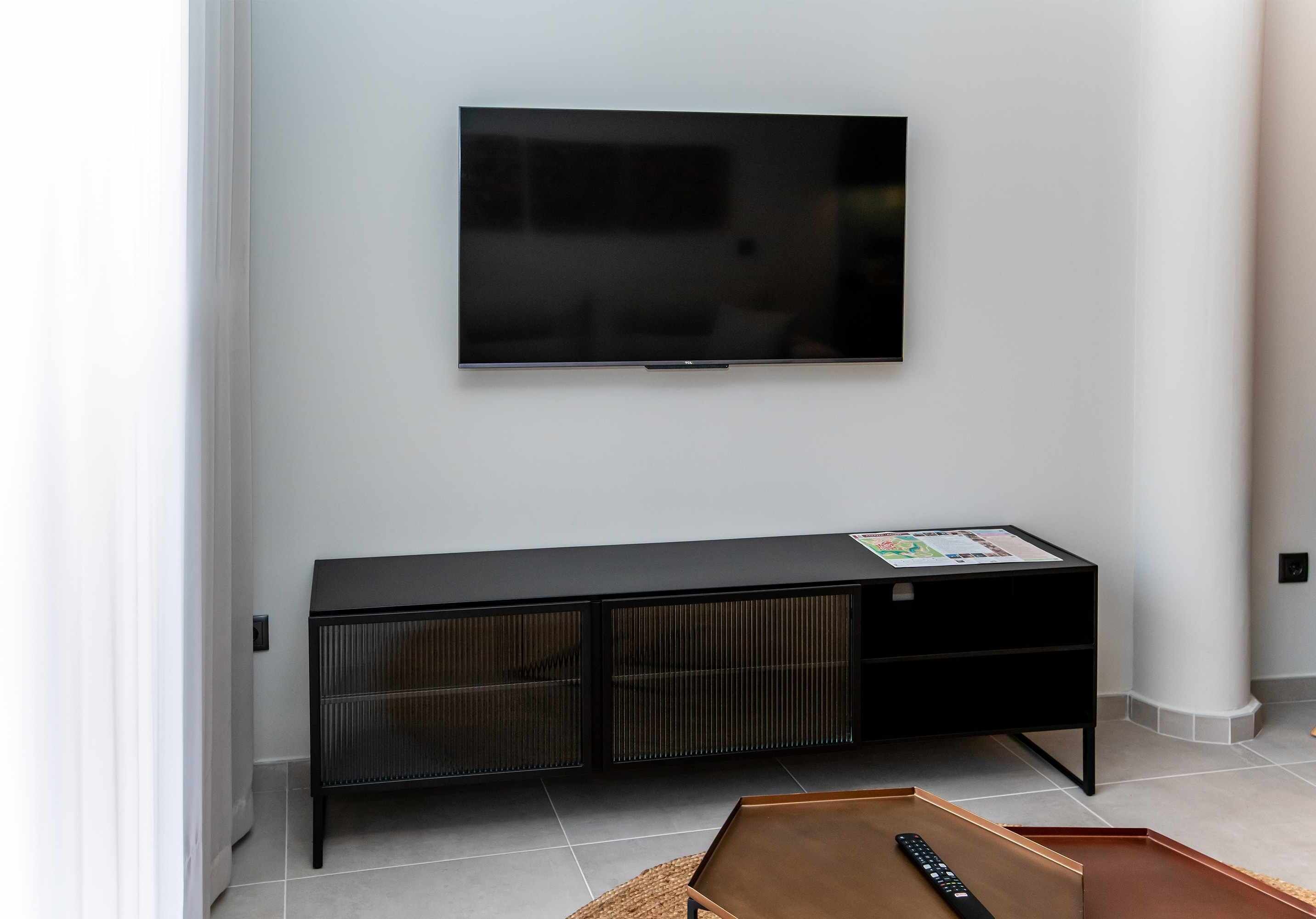 Un soggiorno moderno con una TV a schermo piatto montata a parete, un mobile TV nero con una rivista e un tavolino in legno.