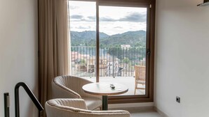A balcony with a view of a cityscape and mountains. There is a round table with a chair and a remote control on it.