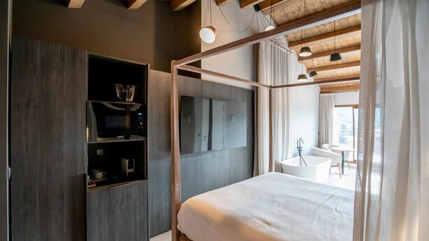 A modern bedroom with a four-poster bed, built-in TV, and a bathroom with a bathtub and sink.
