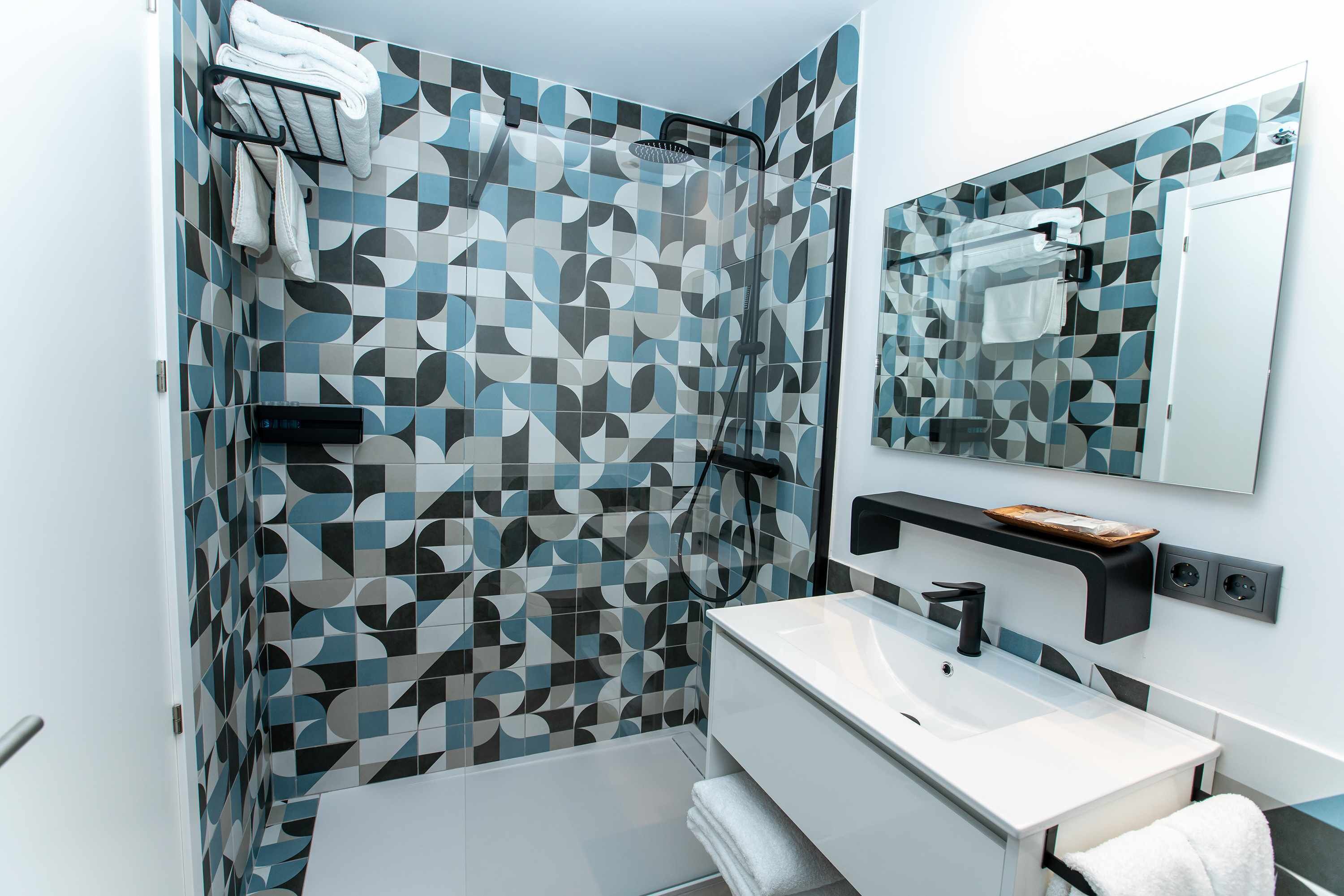 Une salle de bain moderne avec un carrelage aux motifs géométriques, une douche, un lavabo avec un miroir et un porte-serviettes.