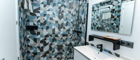 Une salle de bain moderne avec un carrelage aux motifs géométriques, une douche, un lavabo avec un miroir et un porte-serviettes.