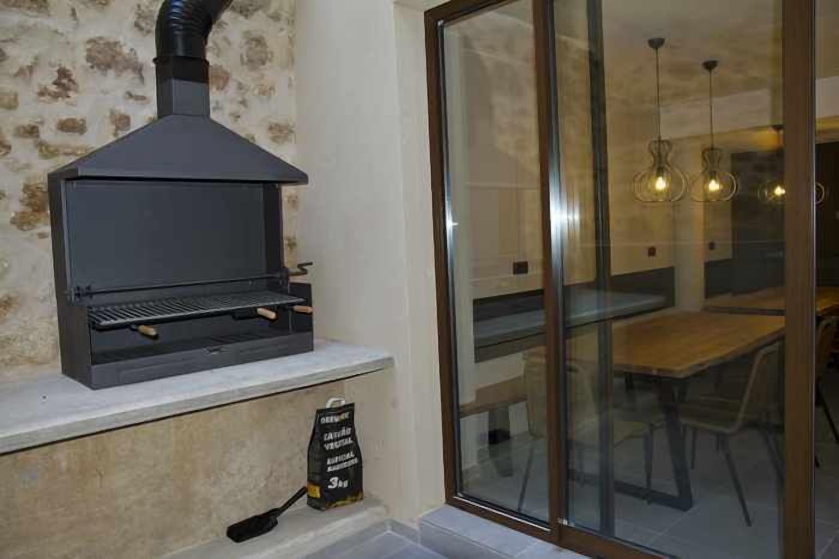 Una cocina moderna con horno de leña empotrado, puerta de cristal que da a un comedor e iluminación colgante.