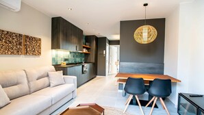 A modern living space with a sofa, dining table, chairs, and a kitchen area. - Mocho-rural-home Lonja A (Beceite)