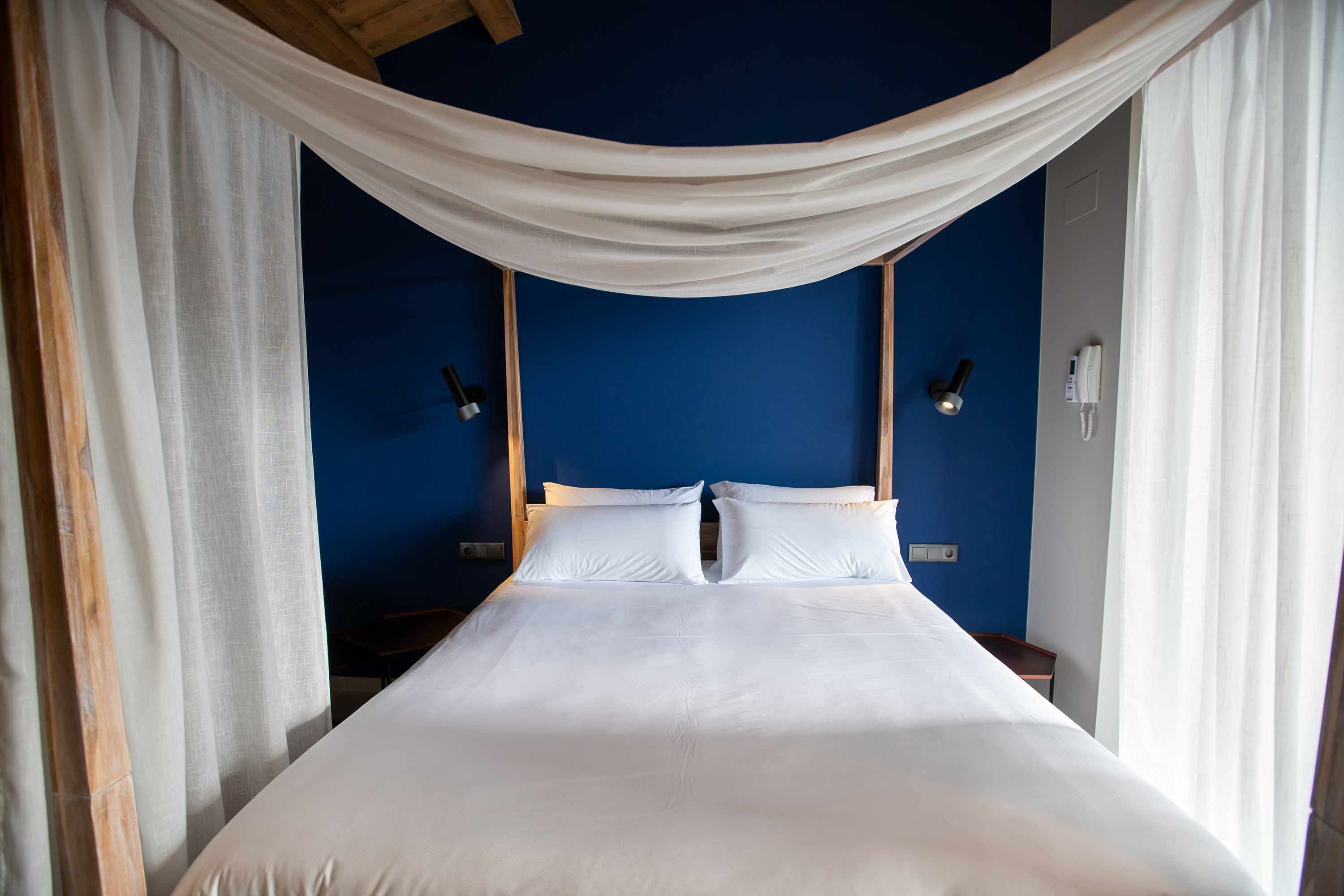 A bed with white bedding, draped white curtains, and two bedside lamps.
