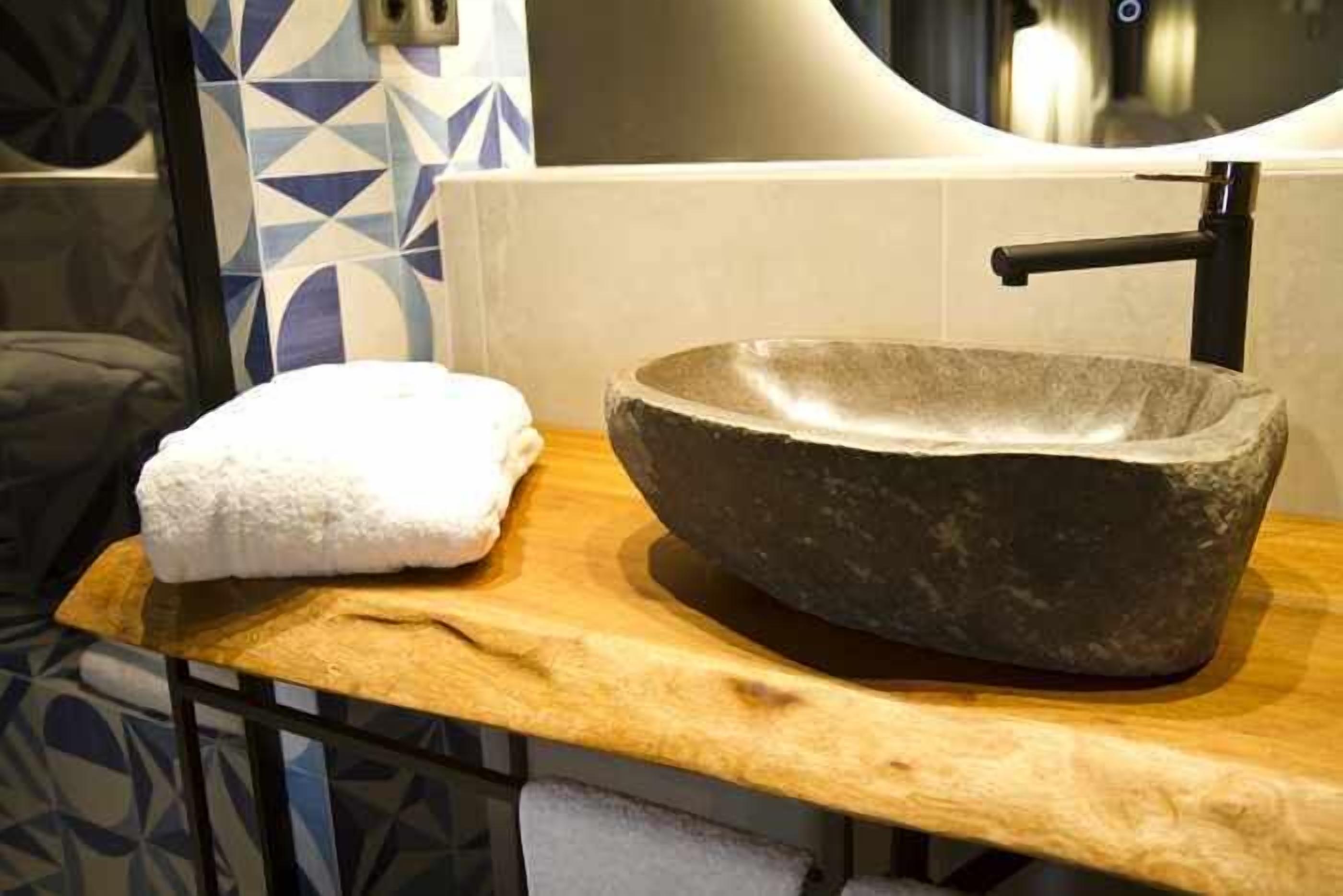 Un lavabo de piedra sobre una encimera de madera, con una toalla a un lado, en un baño con baldosas estampadas.