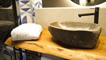 Un lavabo de piedra sobre una encimera de madera, con una toalla a un lado, en un baño con baldosas estampadas.