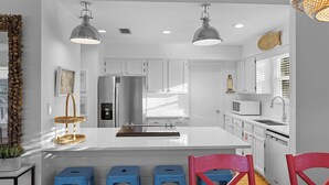 A modern kitchen with white cabinets, a stainless steel refrigerator, a microwave, and a sink. There are three blue stools and a red chair. - Dune Betty - 30A, Heated Private Pool, Walk to the Beach + Restaurants! (Santa Rosa Beach)