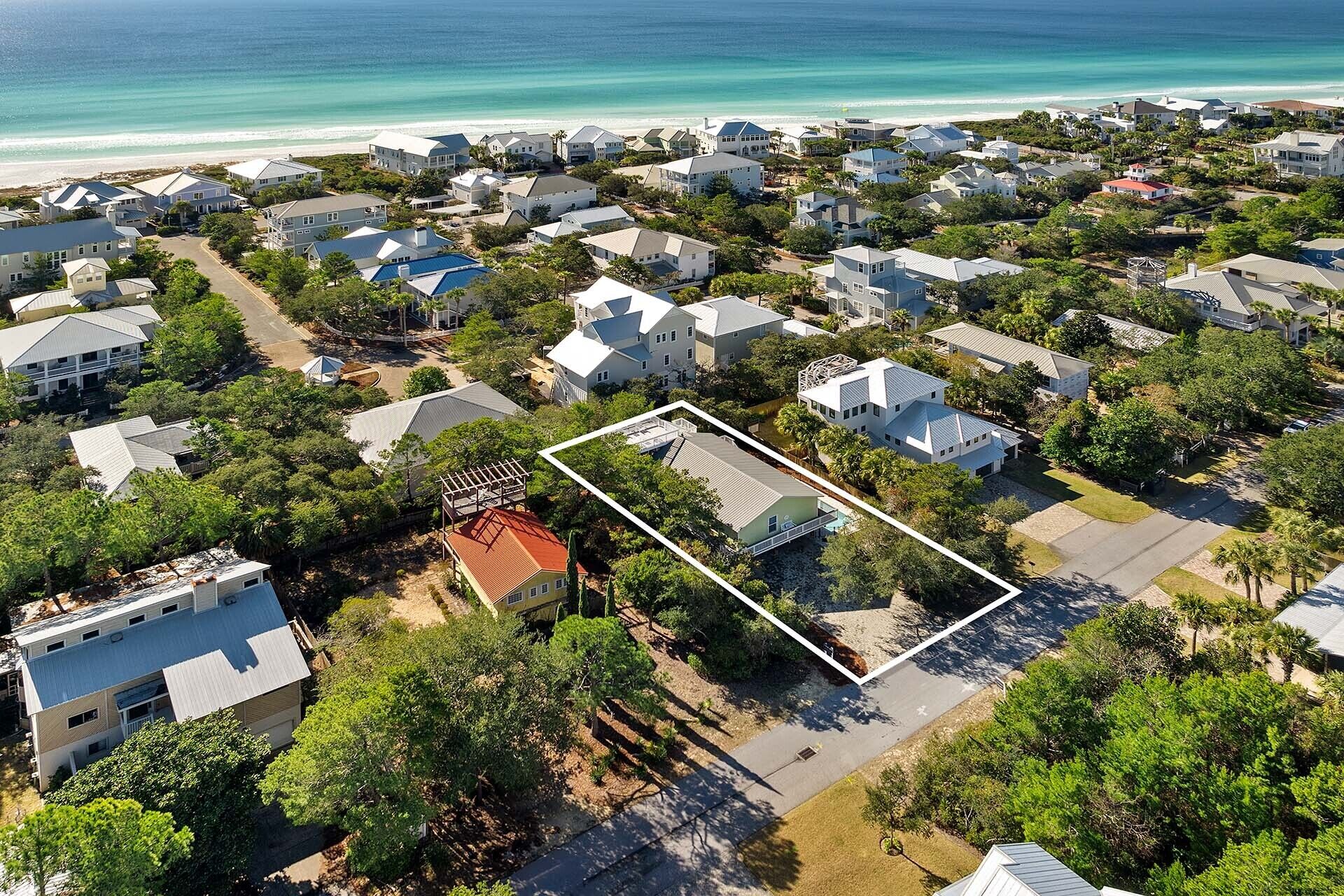 Vue aérienne d’un quartier résidentiel situé sur la côte, avec des maisons, un terrain délimité et une plage en arrière-plan.