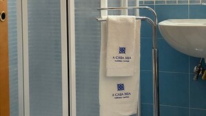 Kylpyhuoneessa on lasiseinäinen suihkukaappi, valkoinen pesuallas ja pyyheteline, jossa on pyyhe.