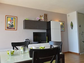 A modern kitchen with a dining table, chairs, a refrigerator, and a television.