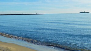 Mare calmo con una spiaggia sabbiosa e un faro in lontananza.