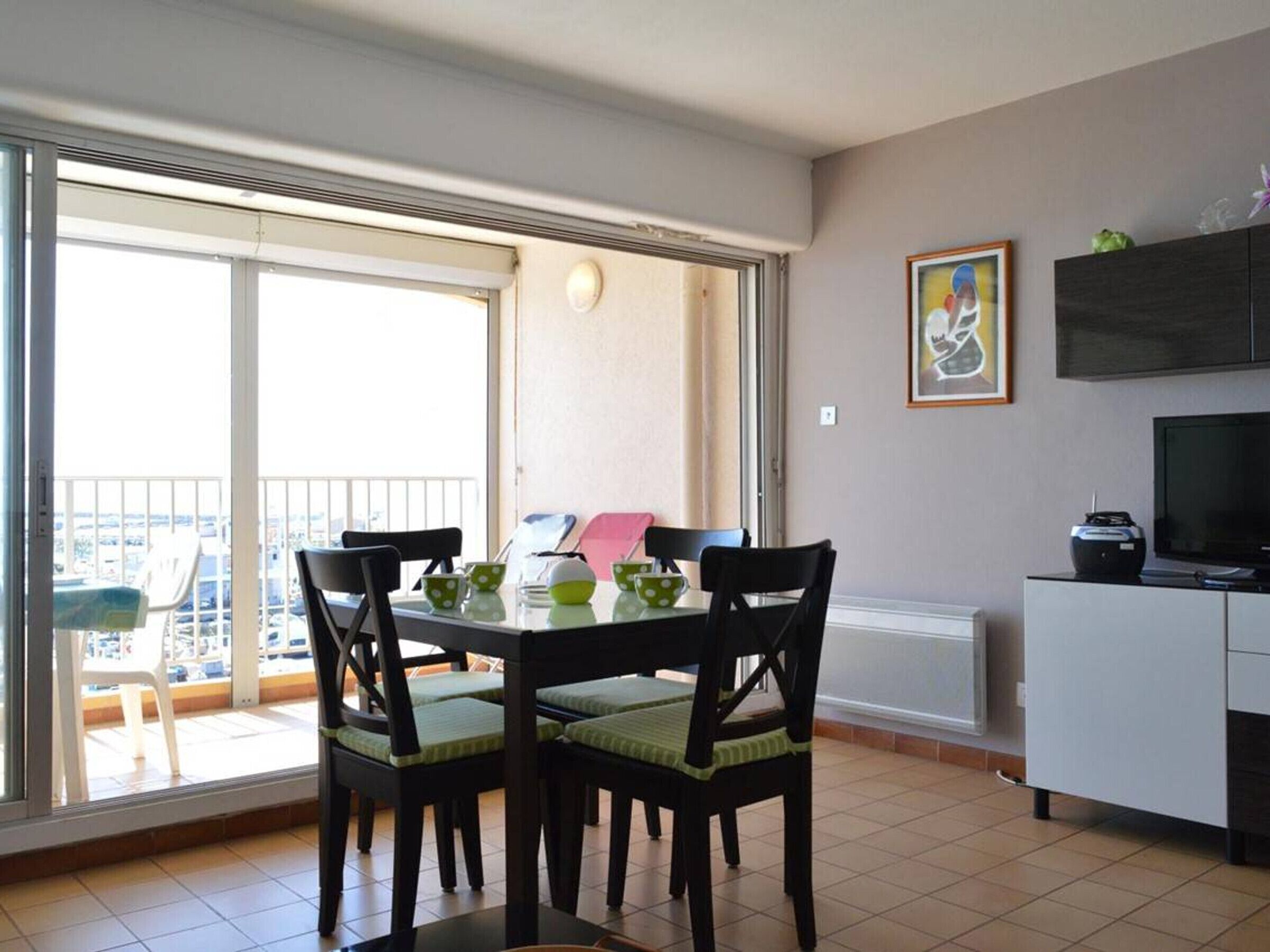 A dining area with a table and chairs, a TV, and a balcony with a view.