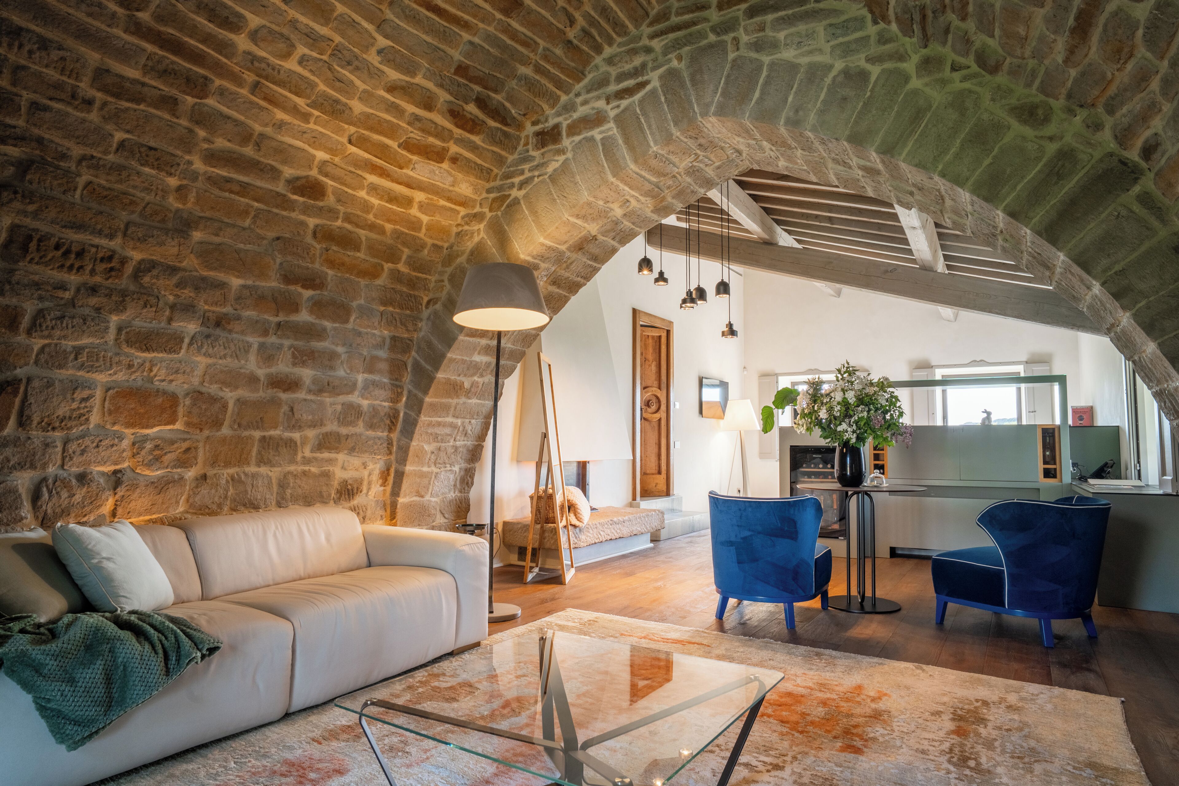 A spacious living area with a stone arch, a sofa, a glass coffee table, and blue chairs.