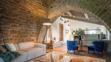 A spacious living area with a stone arch, a sofa, a glass coffee table, and blue chairs.
