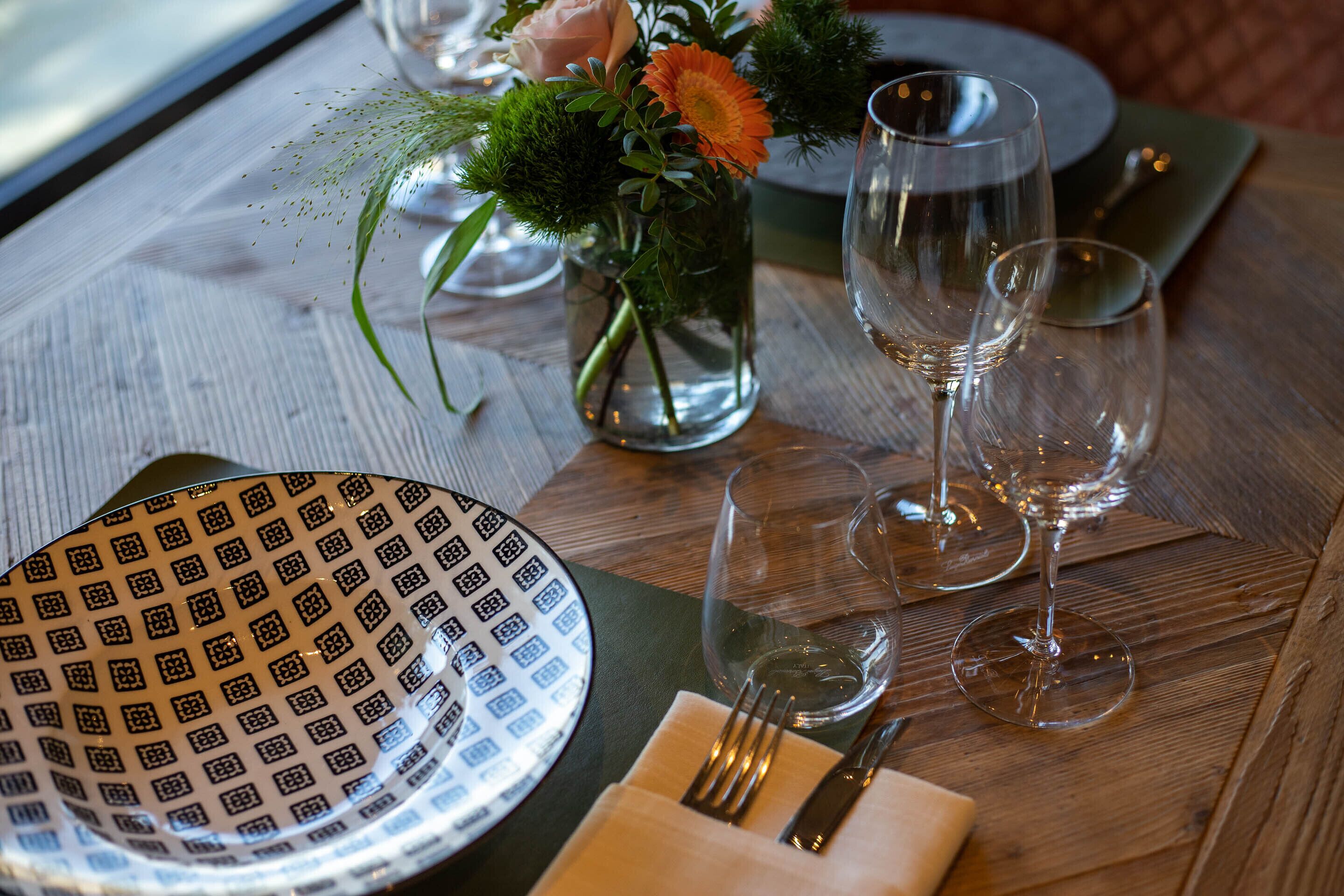 A dining table set with a patterned plate, a vase with flowers, and wine glasses.