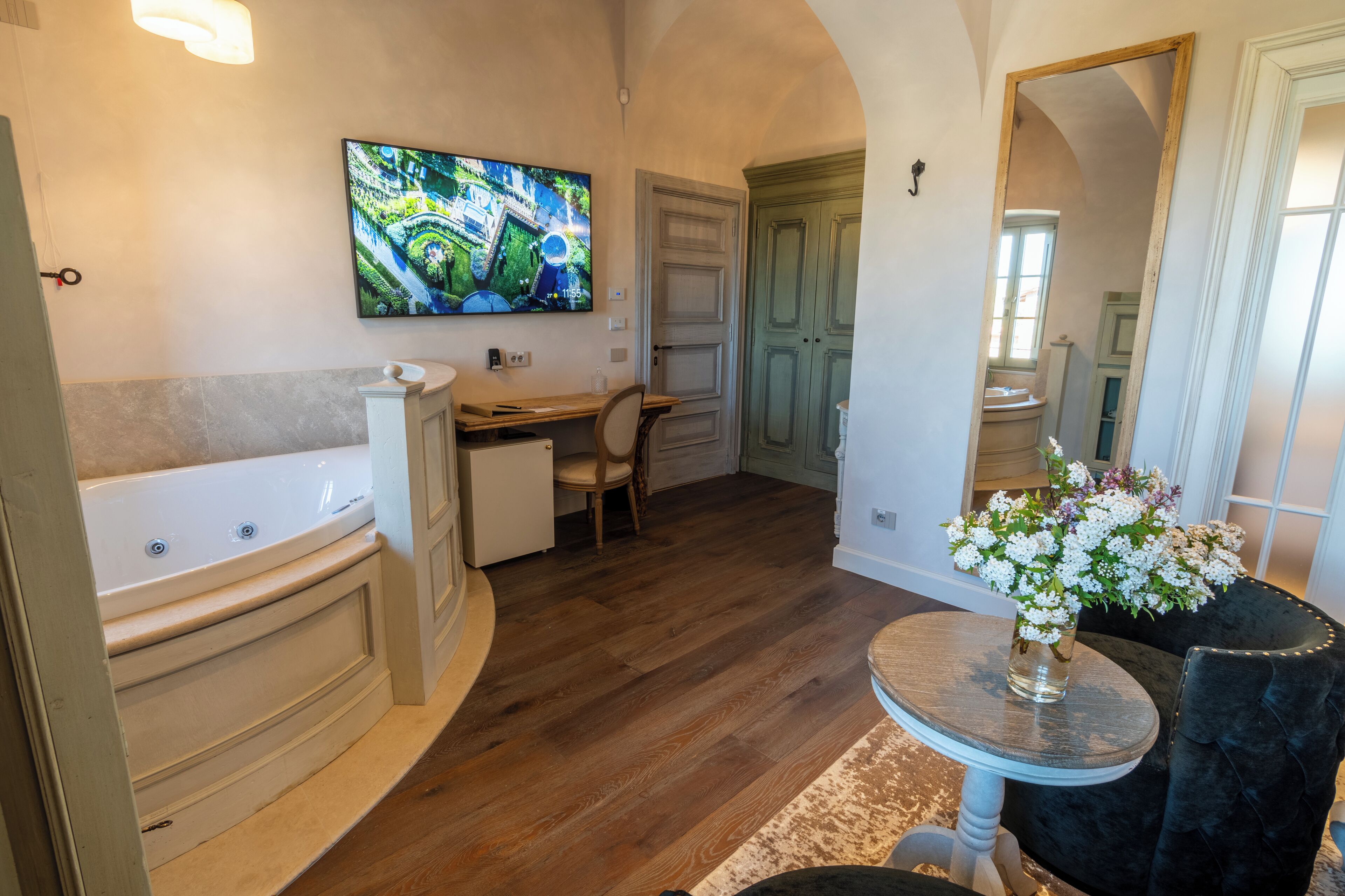 A bathroom with a bathtub, a sink, a mirror, and a television mounted on the wall.