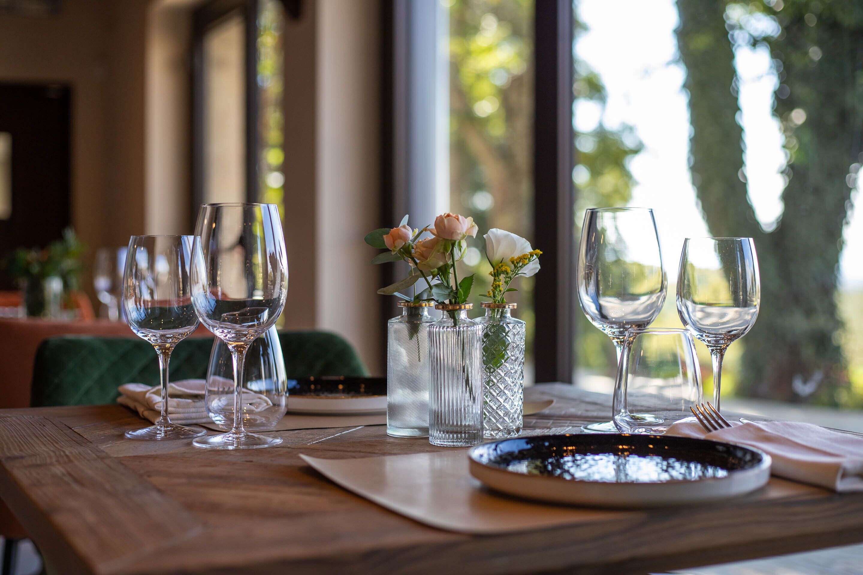 Une table dressée avec des verres à vin, un vase rempli de fleurs et une assiette noire.
