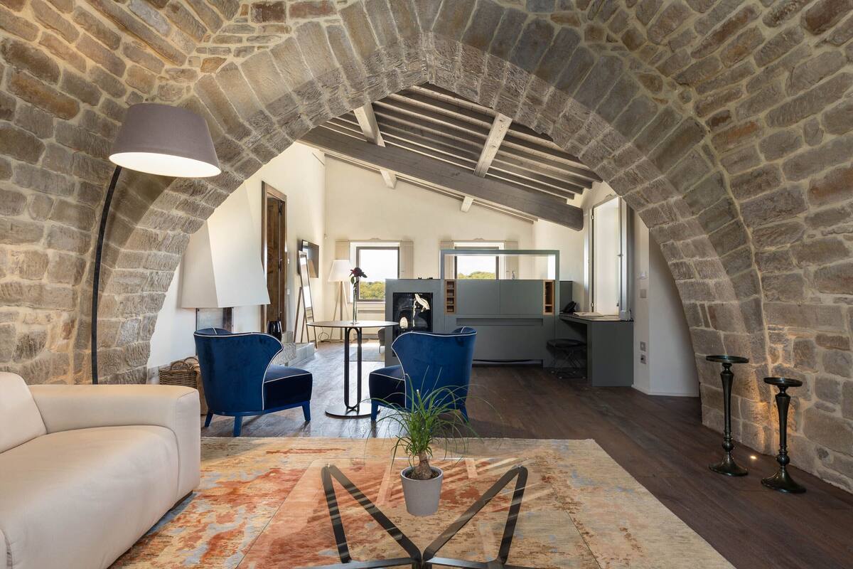 Un loft amplio con paredes de piedra vista, un ventanal grande y una zona de estar acogedora con sofá y sillones.