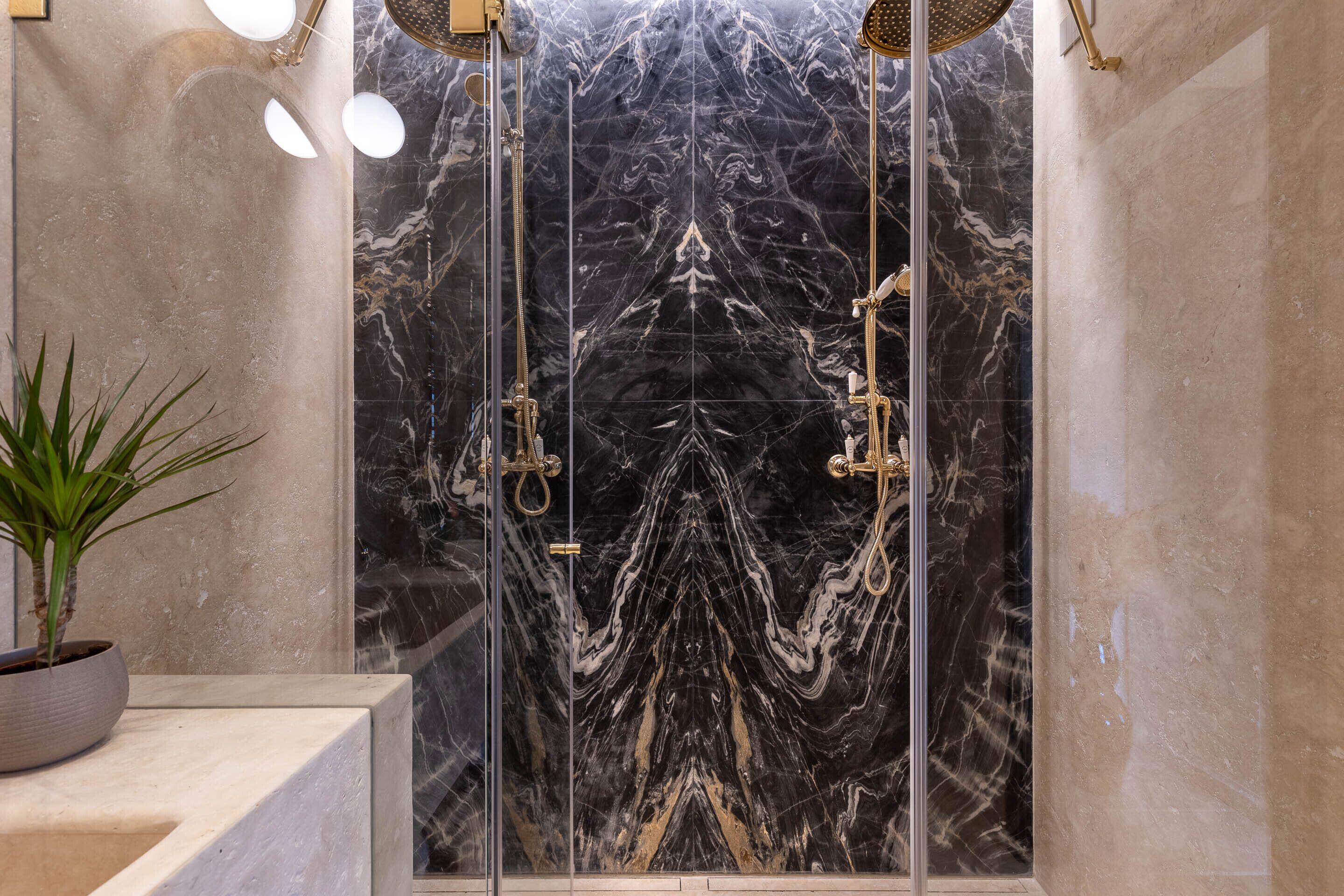 A modern bathroom with a marble shower enclosure, a potted plant, and a marble countertop.