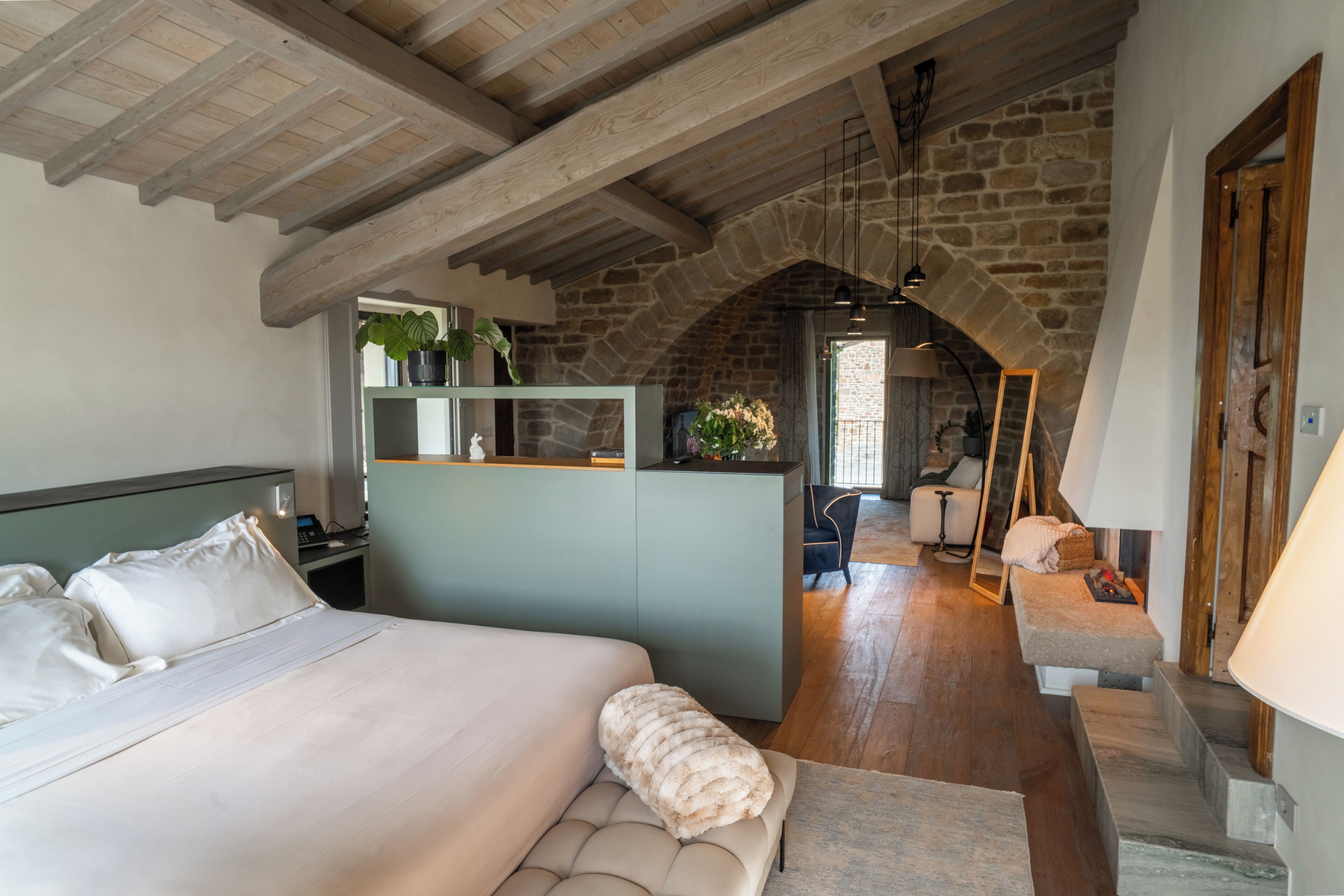 Une chambre à coucher avec un lit, un banc, un bureau et un mur en pierre.