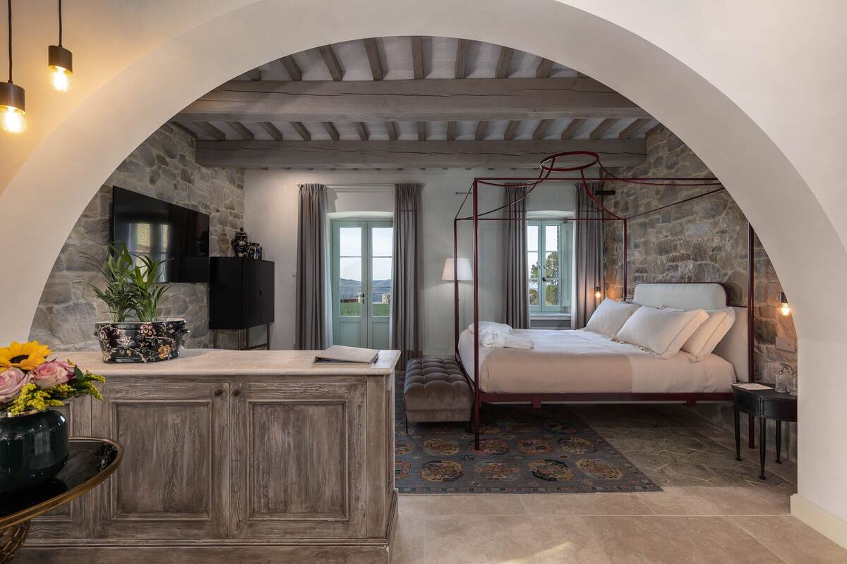 Un dormitorio con pared de piedra, una cama, un tocador y un televisor.