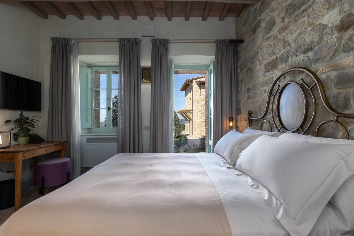 Un dormitorio con una cama grande, un escritorio de madera, un televisor y una pared de piedra.