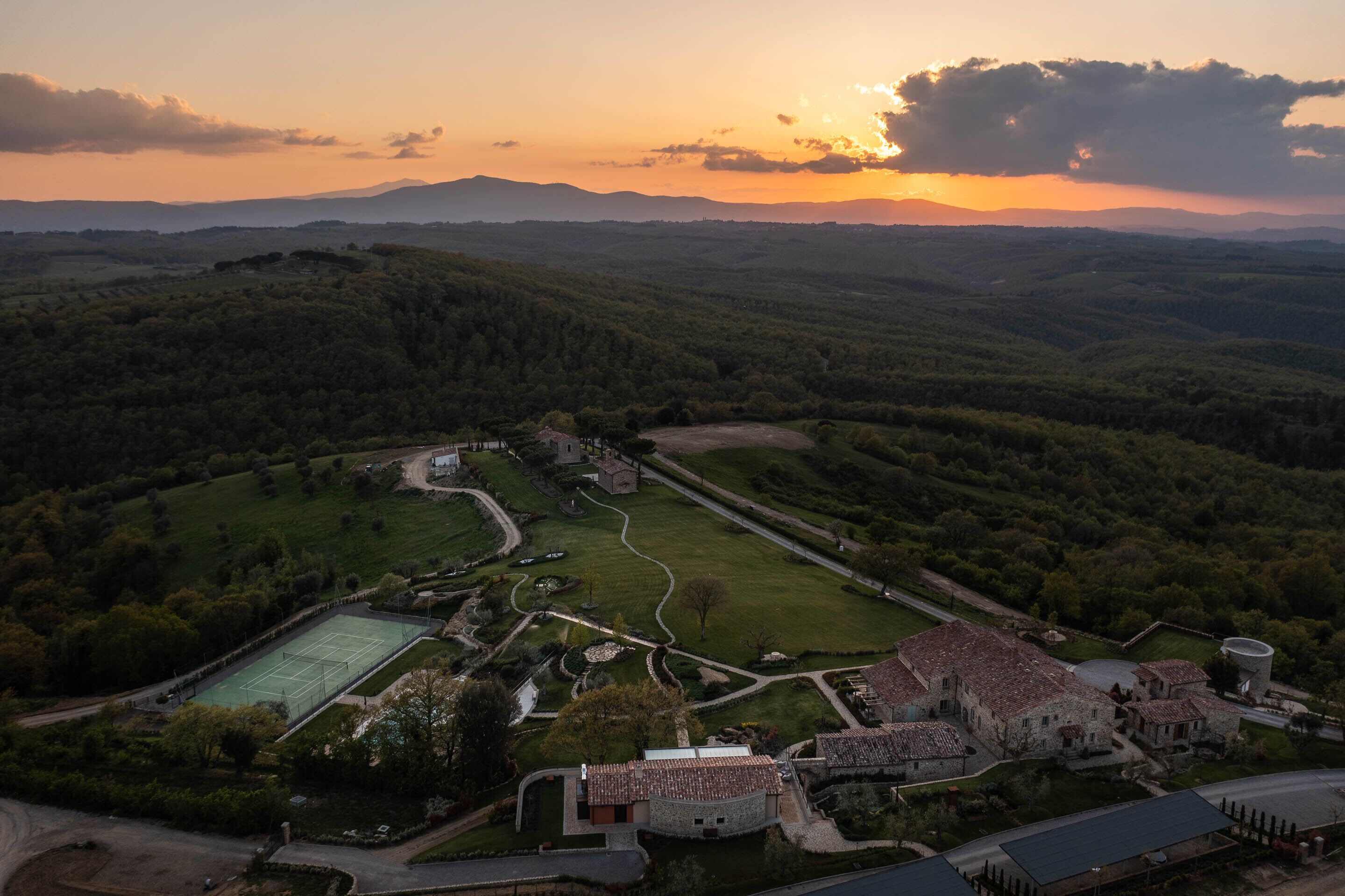 Vista aérea de una finca histórica con cancha de tenis, jardines ajardinados y edificios de piedra tradicionales.