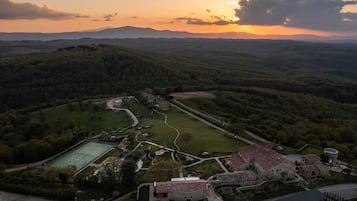 Vista aérea de una finca histórica con cancha de tenis, jardines ajardinados y edificios de piedra tradicionales.