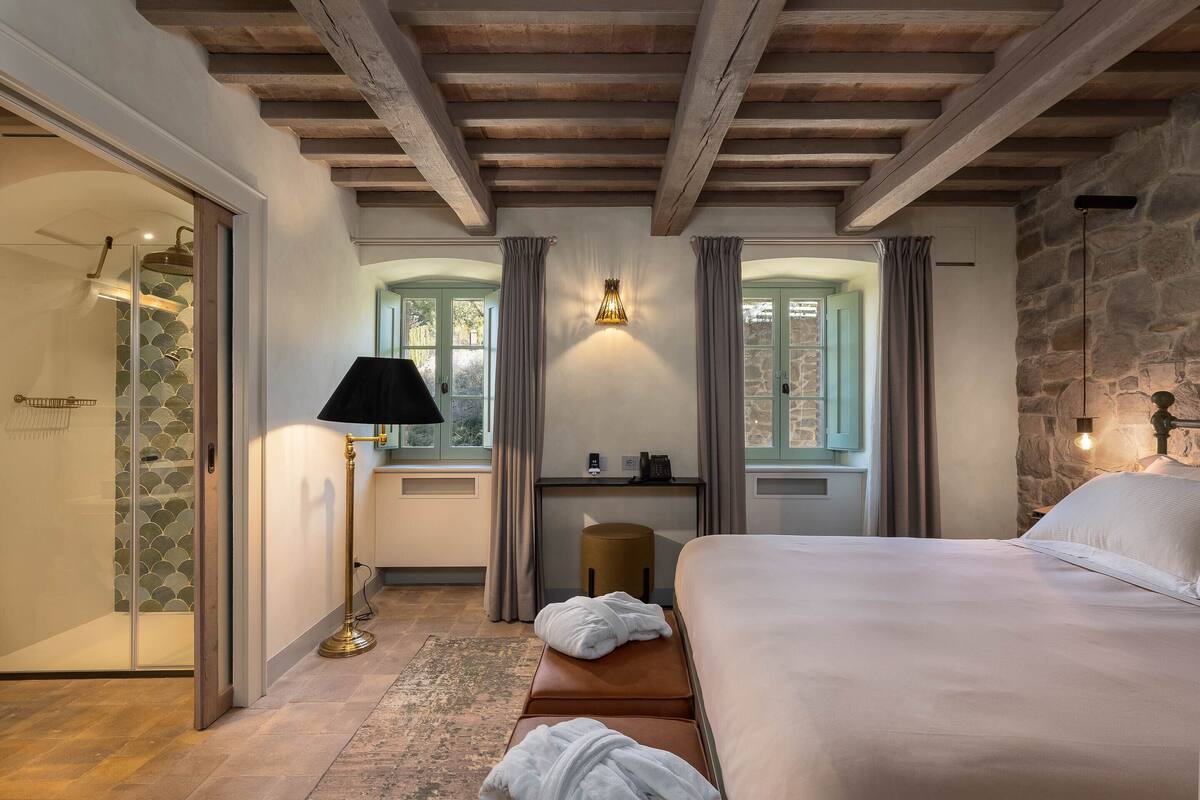 Una habitación de hotel con cama, escritorio, lámpara y pared de piedra.