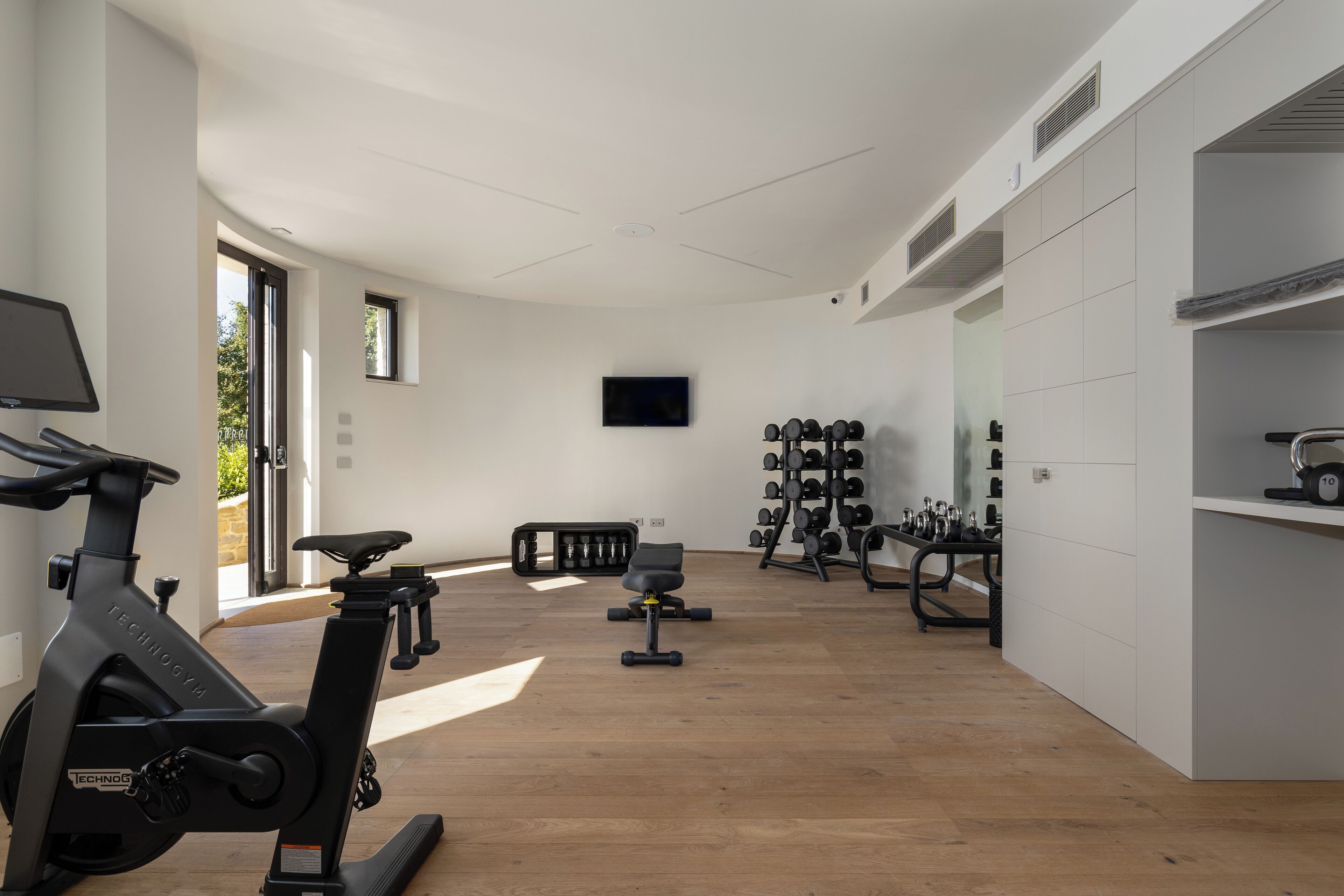 A modern gym with exercise equipment, a television, and a large window.
