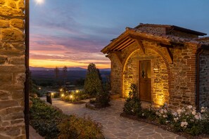 Un edificio de piedra con puerta de madera y arco de piedra, rodeado por un jardín con flores y arbustos.