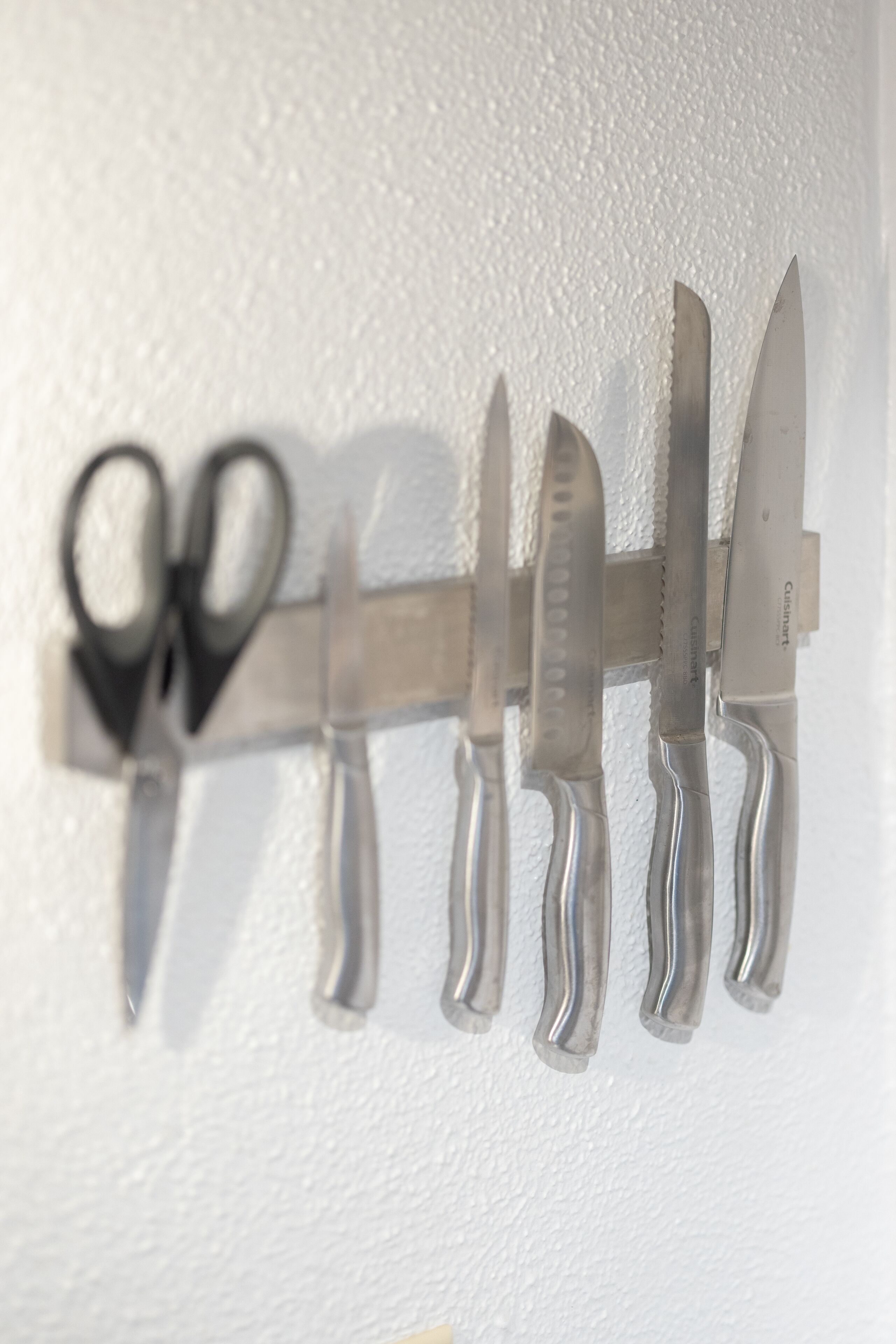 Un porte-couteaux mural avec différents couteaux de cuisine et une paire de ciseaux.