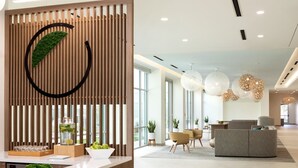 Uma área de recepção moderna com divisória de madeira, vitrine de vidro com objetos decorativos e um espaço de estar com mobiliário contemporâneo.