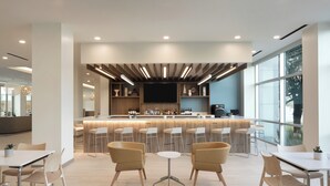 A modern bar area with a long counter, multiple stools, and a large window providing natural light.