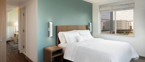 A modern hotel room with a bed, bedside tables, a window with a city view, and a door leading to a hallway.
