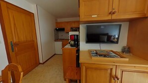 A compact kitchen with wooden cabinets, a small countertop, and a television mounted above it. - 2-room apartment, sleeps 6, terrace, garage, Le Grand-Bornand (Le Grand-Bornand)