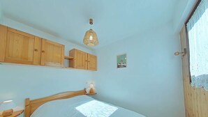 A bedroom with a bed, wooden cabinets, a hanging light fixture, and a small wall decoration. - 2-room apartment, sleeps 6, terrace, garage, Le Grand-Bornand (Le Grand-Bornand)