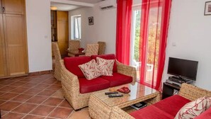Ein Wohnzimmer mit einem roten Sofa, einem Korbtisch und einem Fernseher.
