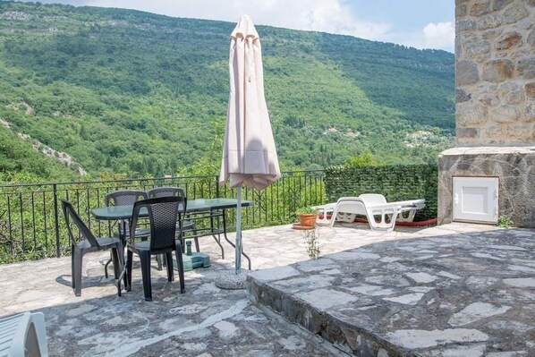 A terrace with a table and chairs, a white umbrella, and a stone wall.