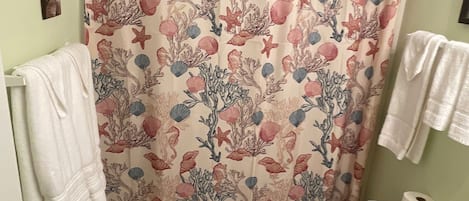 Un baño con suelo de baldosas, un inodoro, una cortina de ducha con estampado floral y un perchero con toallas.