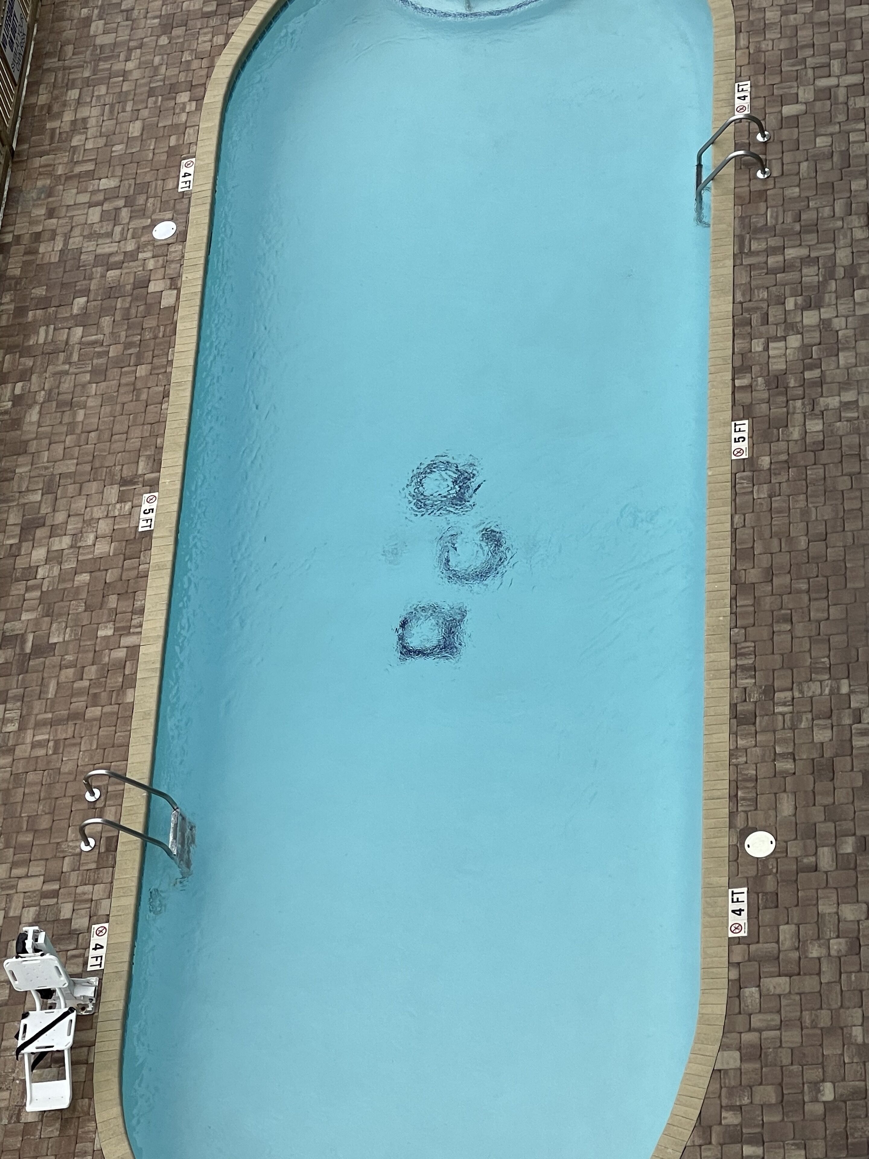 A rectangular swimming pool with a brick border, surrounded by lounge chairs and a tiled deck.