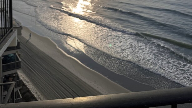 A view of the ocean from a balcony with a railing, waves, and sunlight reflecting on the water. - Family Friendly Fully Equipped two bedrooms two bathrooms Condo in garden city (Murrells Inlet)