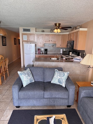 A living room with a grey sofa, a coffee table, and a dining area with chairs.