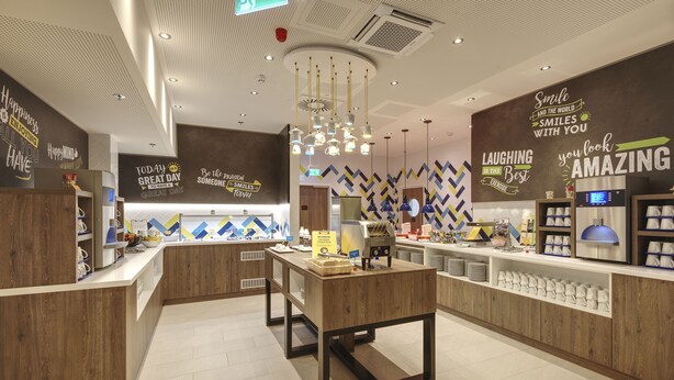 Un caffè moderno con arredi in legno, un tavolo centrale e decorazioni motivazionali alle pareti.