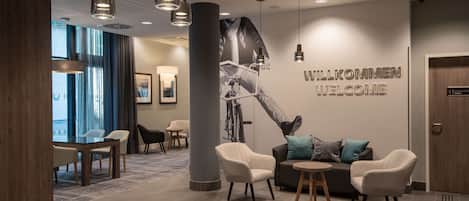 A modern lobby with a 'WELCOME' sign, a large bicycle mural, and a seating area with a round table and chairs.