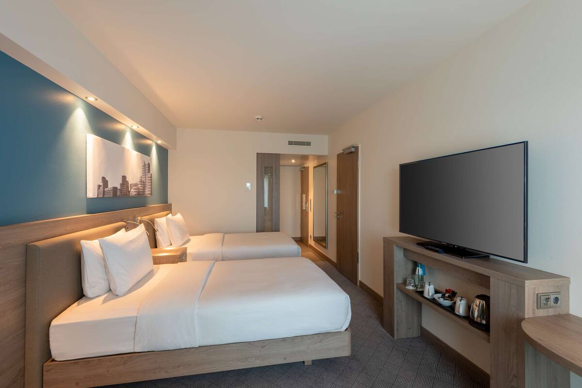 A hotel room with two beds, a TV, and a shelf with toiletries.
