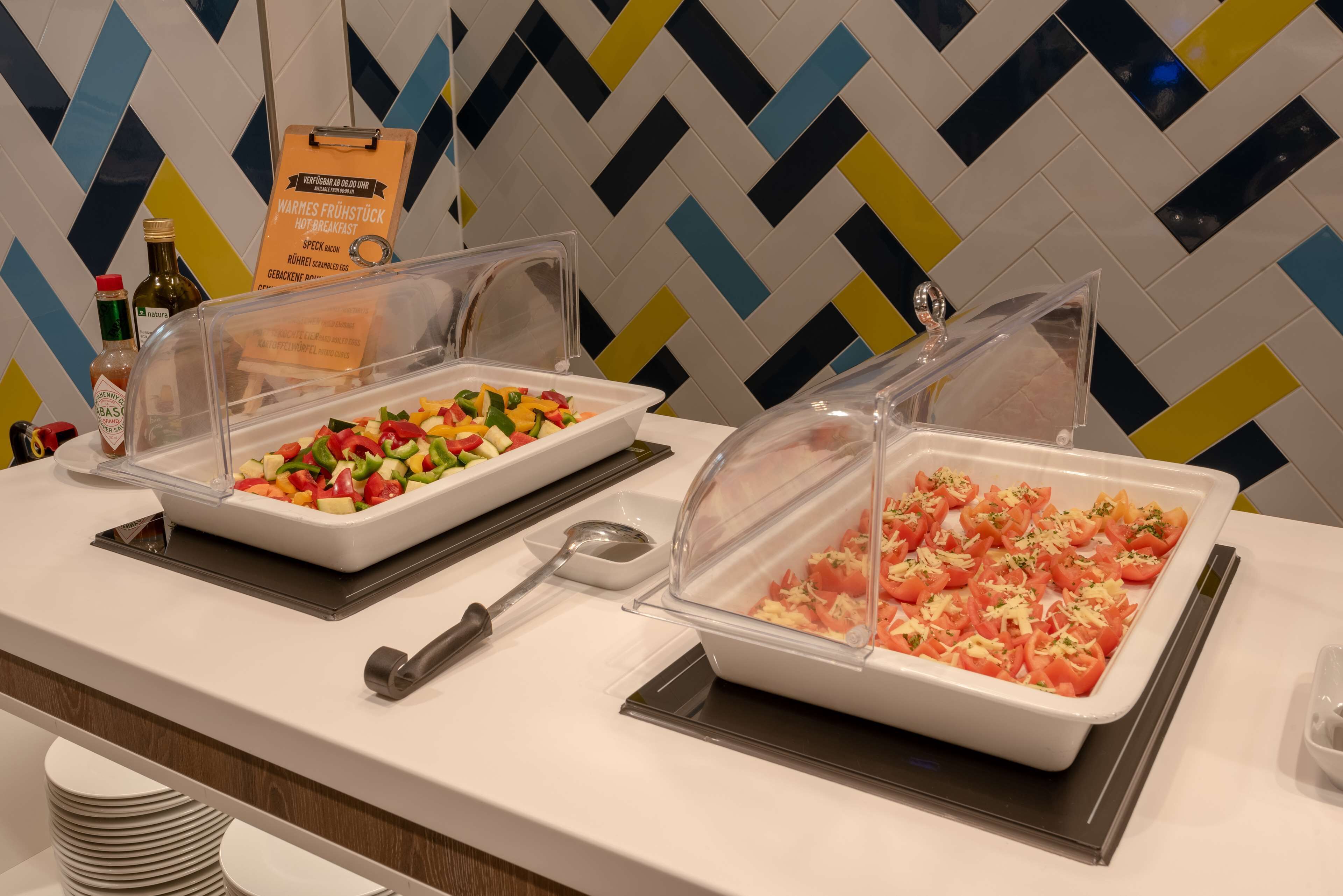 A buffet with covered food containers, including a salad and a dish with tomatoes and cheese.