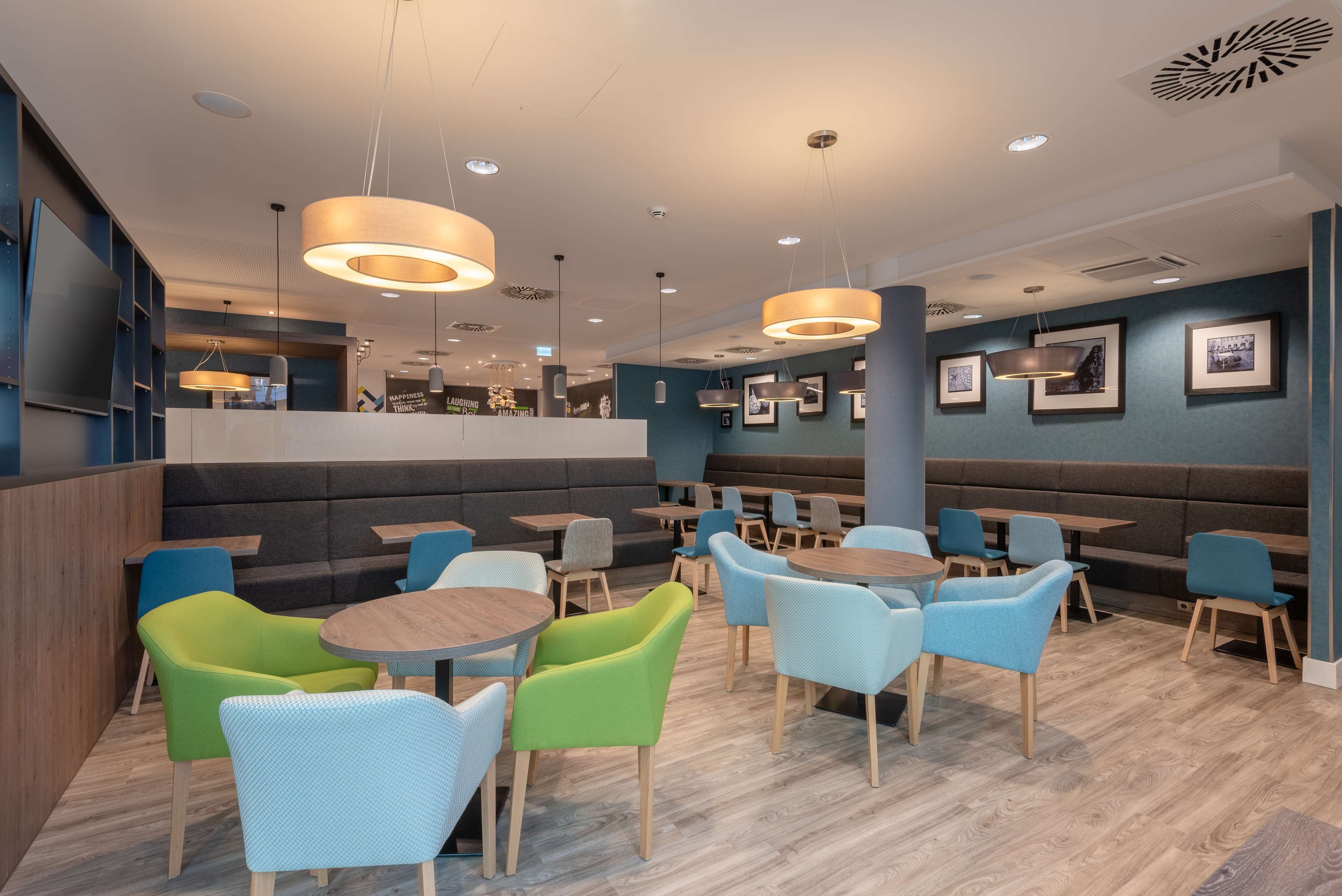 En modern restaurang med runda bord och färgglada stolar, infälld belysning och inramade tavlor på väggarna.
